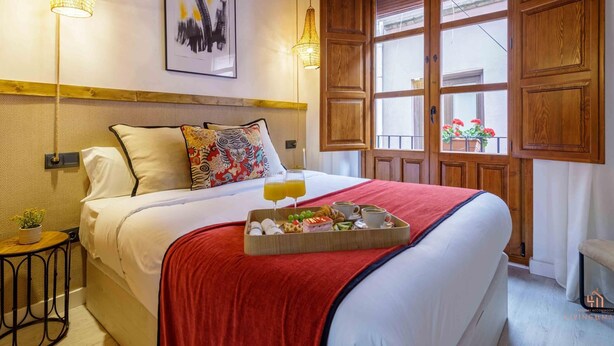 A hotel room with a bed, a tray of breakfast, a painting, and a large window with wooden shutters. - Rustic Chic Living4Malaga (Málaga)