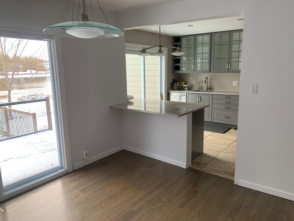 A modern kitchen with a large island, light wood flooring, and a view of a snowy outdoor area.