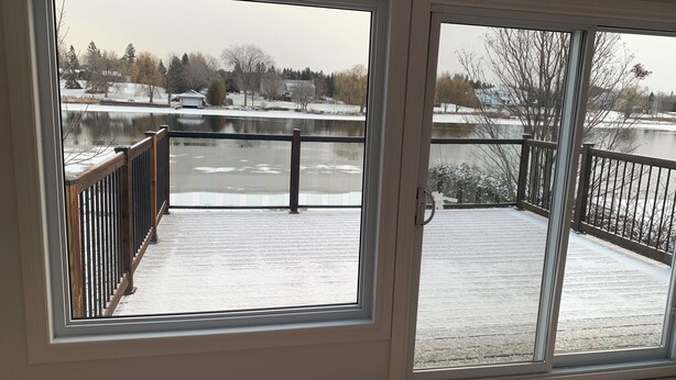 A room with a sliding glass door leading to a balcony with a view of a lake and houses. - Manotick waterfront property. Walking distance to pubs restaurants. groceries.
 (Ottawa)