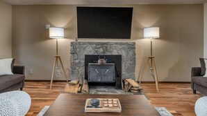 A living room with a stone fireplace, two floor lamps, a wooden coffee table, and a flat-screen TV mounted above the fireplace.