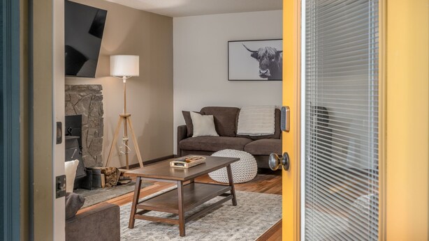 A cozy living room with a stone fireplace, a brown sofa, a wooden coffee table, and a lamp.