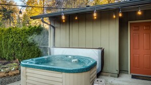 A hot tub in front of a building with a door and string lights.
