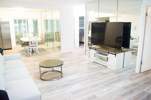A modern living room with a flat-screen TV, a glass partition, a dining area with chairs, and a sofa.