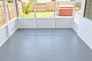 A room with a grey floor, white walls, and a wooden fence visible through a window.