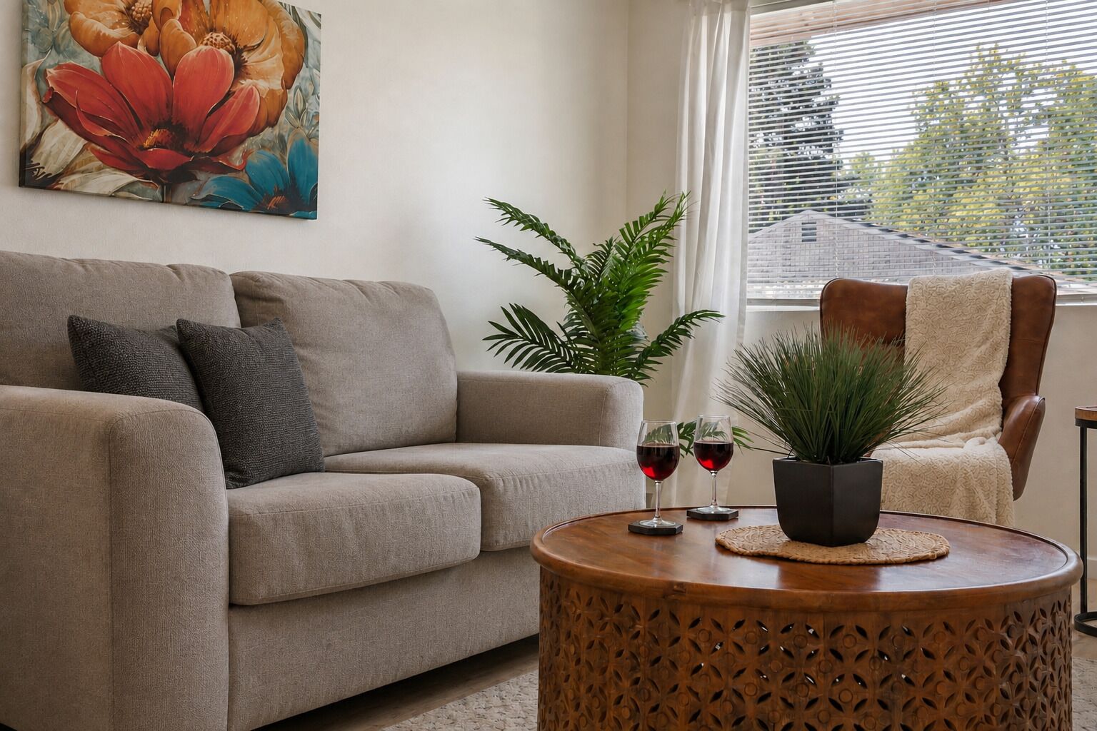Een woonkamer met een bank, een salontafel, een plant in pot en een stoel. Op tafel staan twee wijnglazen.