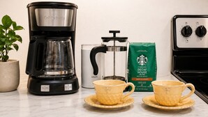 Een koffiezetapparaat, een Krups koffiepers, een zakje Starbucks decaf koffie en twee gele bekers op een aanrecht.