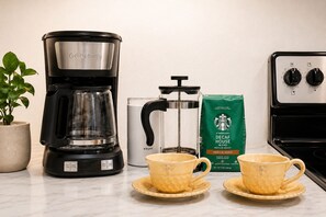 En kaffebryggare, en kaffepress från Krups, ett paket med koffeinfritt kaffe från Starbucks och två gula muggar på en köksbänk.