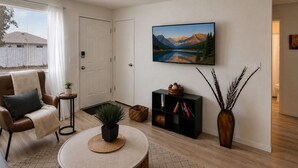 En stue med sofa, sofabord, bogreol, et maleri og en vase med planter.