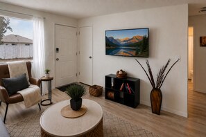 A living room with a sofa, a coffee table, a bookshelf, a painting, and a vase with plants. - Comfy Retreat - Very Quiet - King Bed - Minutes to Kadlec Hospital & PNNL (Richland)