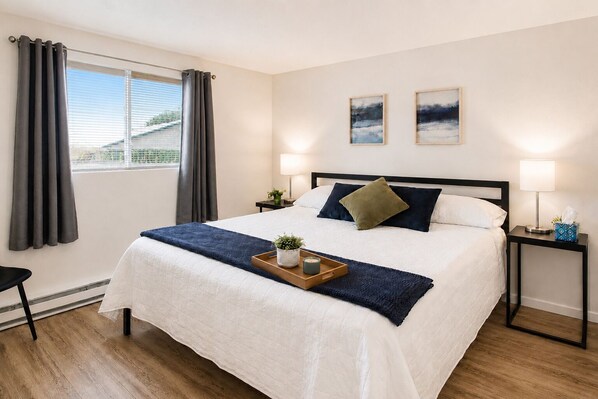 Una habitación de hotel con una cama, dos mesitas de noche, un ventanal con cortinas y dos cuadros colgados en la pared.