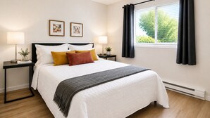 Een keurig opgemaakt slaapkamer met een bed, twee nachtkastjes, een raam met gordijnen en twee ingelijste foto's aan de muur.