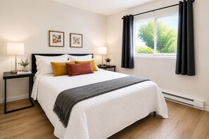 Un dormitorio ordenado con una cama, dos mesitas de noche, un ventanal con cortinas y dos cuadros en la pared.