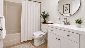 Een badkamer met douchegordijn, toilet, wastafel, spiegel en een potplant.