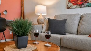 En stue med en sofa, to vinglas, en potteplante, en lampe og et maleri på væggen.