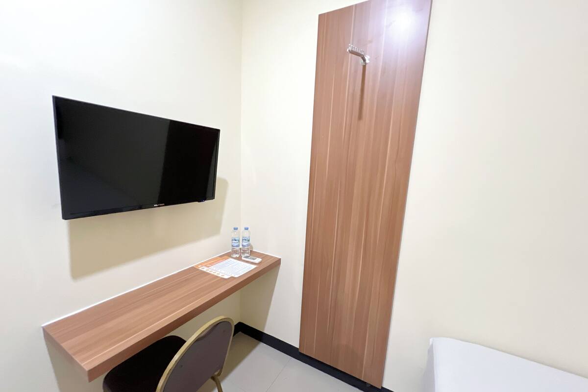 A small room with a wooden desk, a chair, a flat-screen TV mounted on the wall, and a wooden door.