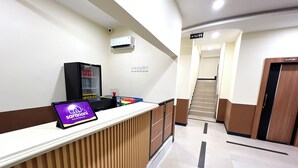 A hotel reception area with a reception desk, a digital screen displaying 'sarani', a vending machine, and a staircase leading to the upper floors. - Wisma Saranani (Kendari)
