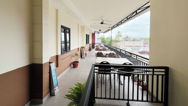 A covered corridor with tables and chairs, potted plants, and a view of the street. - Wisma Saranani (Kendari)