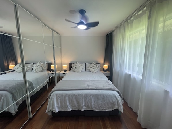 Une chambre d’hôtel avec un grand lit, deux tables de chevet avec des lampes, un ventilateur de plafond et un grand miroir.
