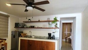 A kitchen with a central island, wooden cabinets, a refrigerator, a microwave, a coffee maker, and a ceiling fan. - Las Huayitas by Casa Amaranto (Mérida)