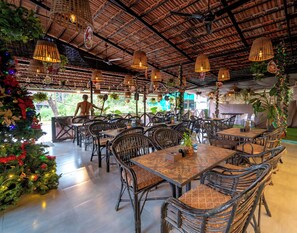 A restaurant with wicker furniture, hanging lights, and a Christmas tree.