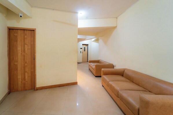 A spacious living area with a wooden door, a beige sofa, and a tiled floor.