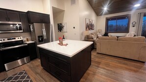 Una cocina moderna con electrodomésticos de acero inoxidable, una isla central y una sala de estar con sofá y ventana.
