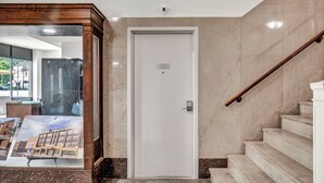 Recepció d'hotel amb una escalinata de marbre, una porta blanca amb el número 101, i una paret de vidre que mostra un model d'edifici.