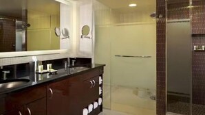 A modern bathroom with a large mirror, two sinks, a shower enclosure, and a vanity with drawers. - Luxury Hilton Elara ON THE STRIP (Las Vegas)