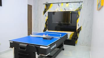 Una mesa de ping pong en una habitación con piso de mármol y una gran pantalla de televisión en la pared.
