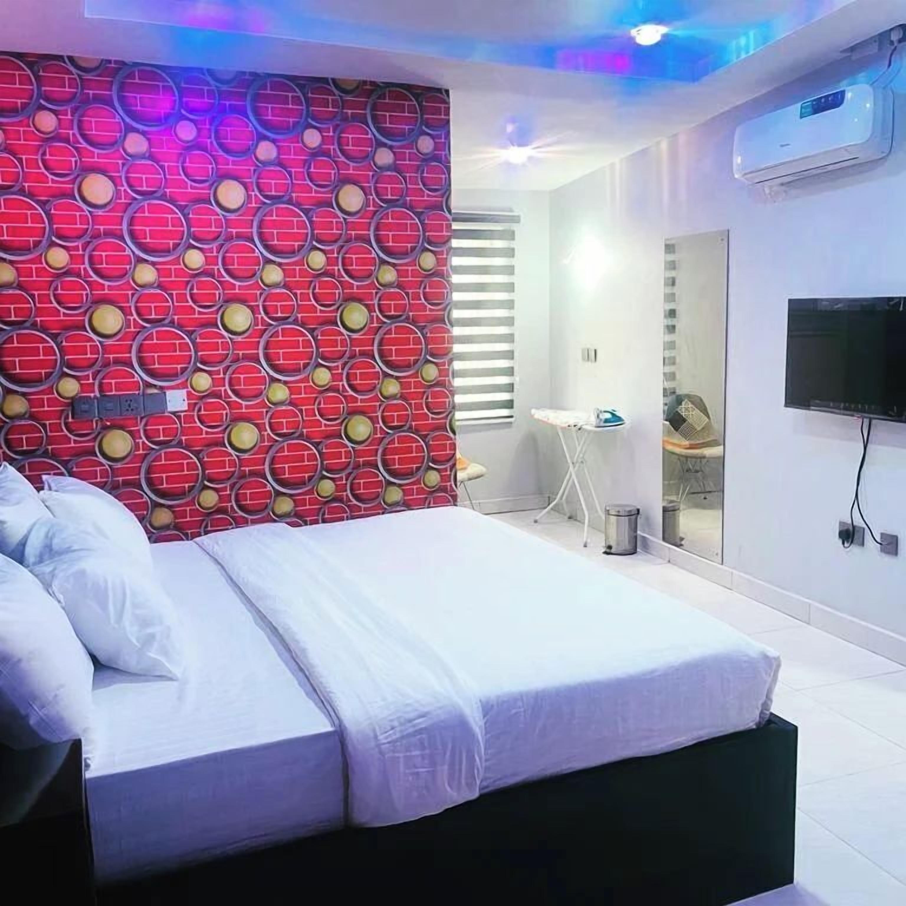 A modern bedroom with a bed, a TV, and a bathroom visible in the background.