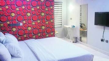 A modern bedroom with a bed, a TV, and a bathroom visible in the background.