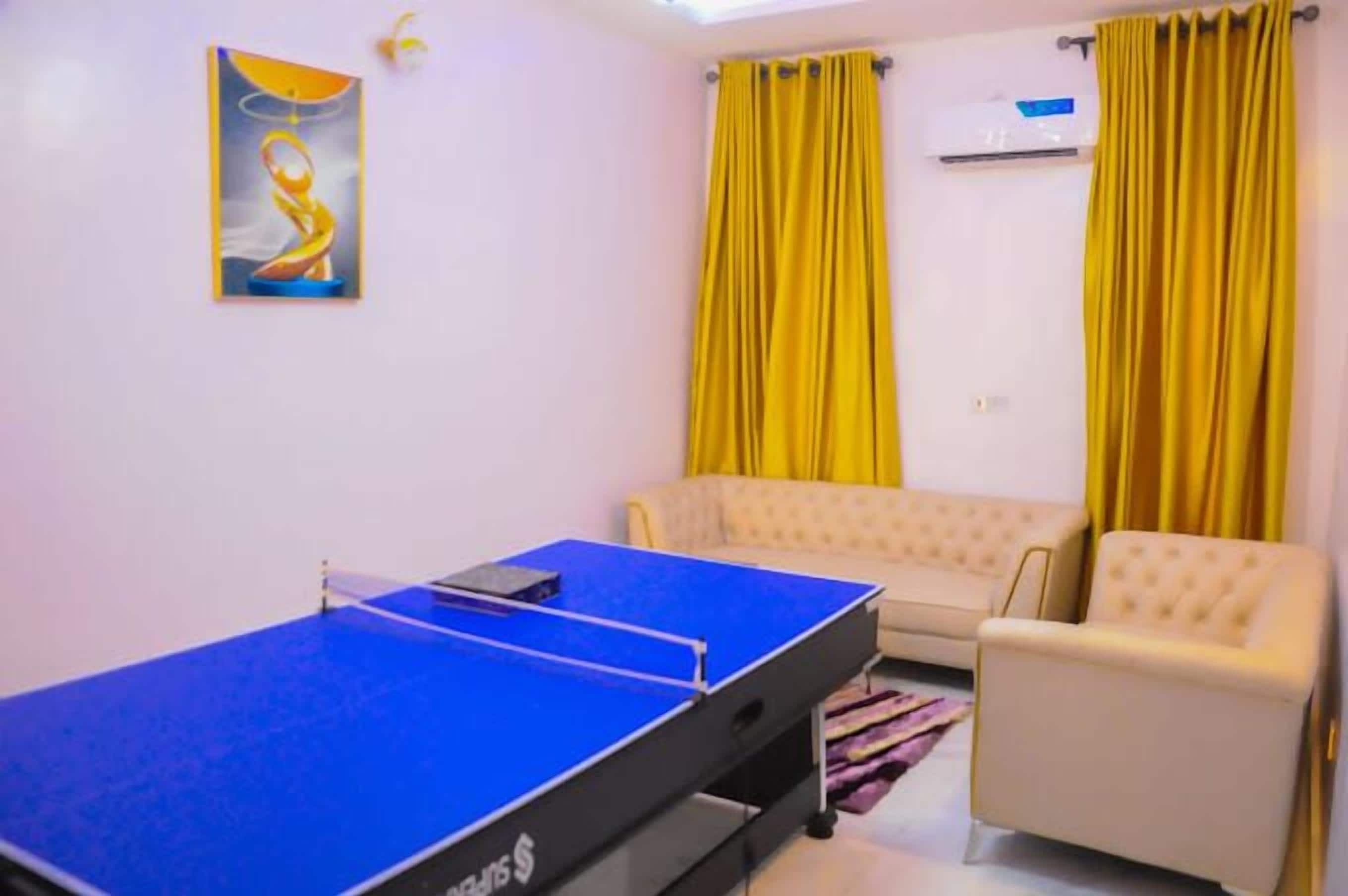 A room with a ping pong table, a sofa, and yellow curtains.