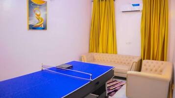 A room with a ping pong table, a sofa, and yellow curtains.