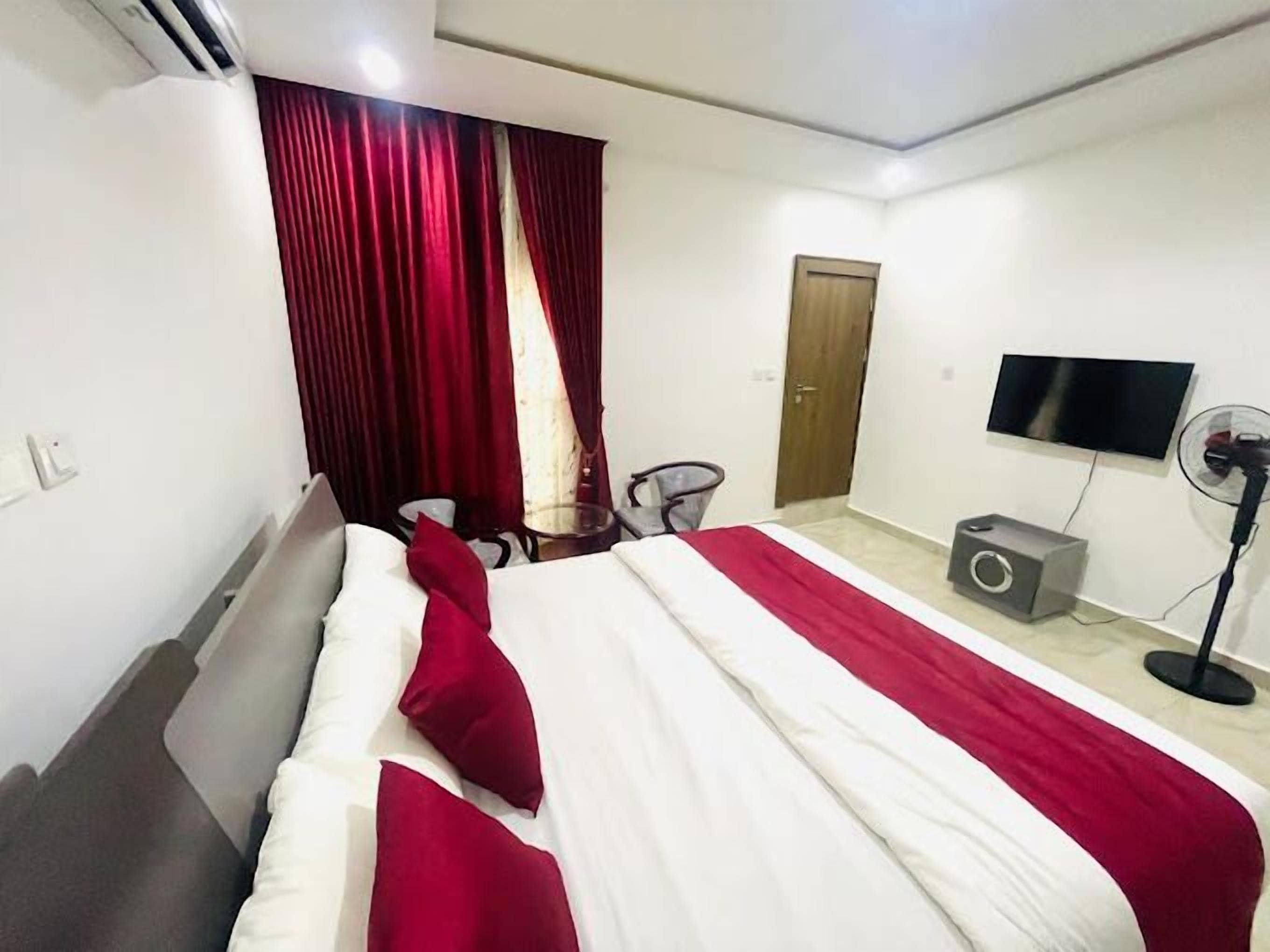 Una camera d'albergo con un letto, una scrivania, una sedia, una televisione e una ventola.