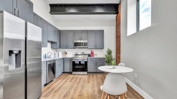 A modern kitchen with grey cabinets, stainless steel appliances, and a wooden floor.