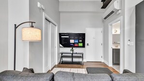 A modern living room with a flat-screen TV mounted on a wall, grey sofas, a floor lamp, and a console table.