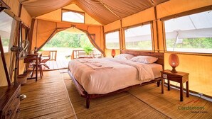 Una habitación de campamento con carpa, una cama, un ventilador, una mesa y una lámpara.