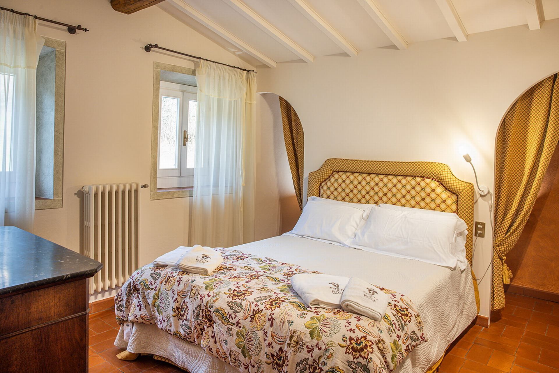 Une chambre à coucher avec un lit, une fenêtre avec des rideaux, un radiateur et un plafond en bois.