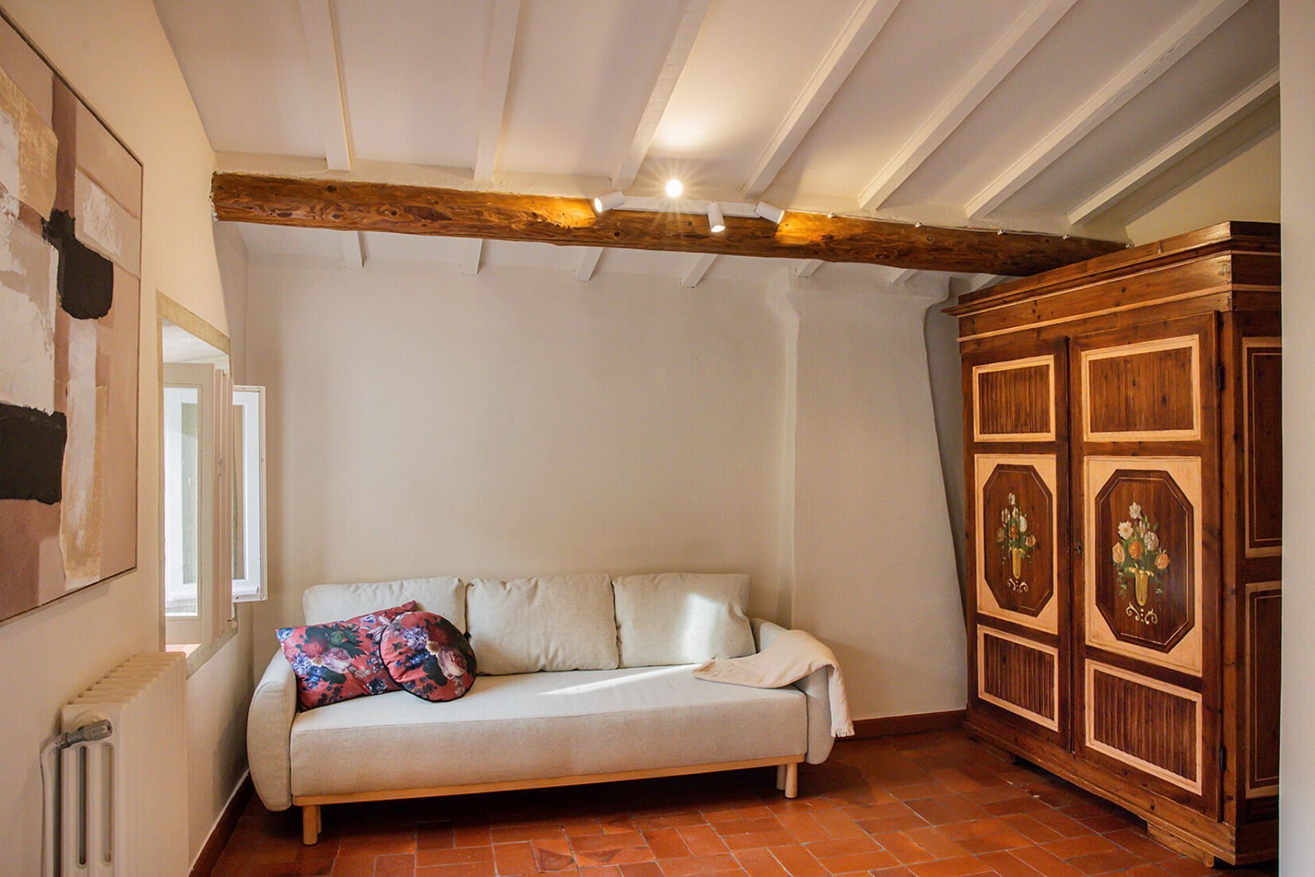A room with a sofa, a radiator, a wooden cabinet, and a ceiling with exposed beams.