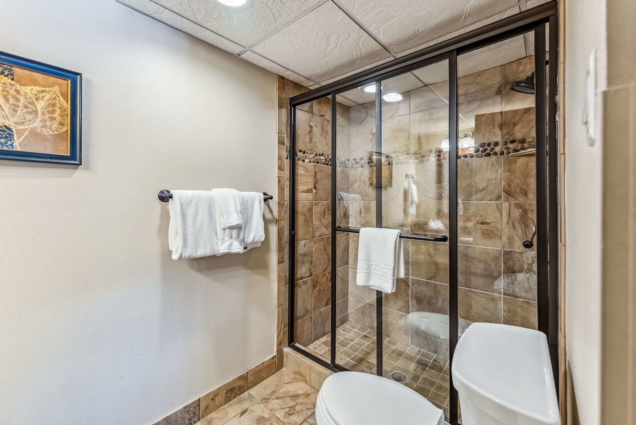 A modern bathroom with a glass-enclosed shower, a toilet, and a towel rack with white towels.