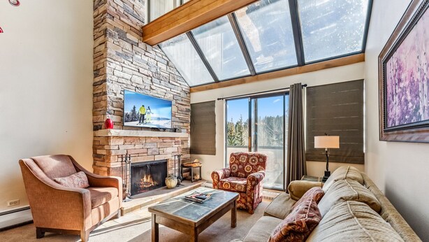 A cozy living room with a fireplace, comfortable seating, and large windows offering a view of the outdoors. - Breck Ski-In/Ski-Out Condo with Resort Amenities (Breckenridge)