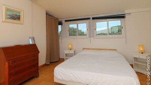 Ein Schlafzimmer mit einem Bett, einem Schminktisch, zwei Nachttischen mit Lampen, einem Fenster mit Aussicht und einer Tür.