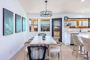 A modern kitchen with a dining area, featuring a large window, a hanging light fixture, and a view of the outdoors.