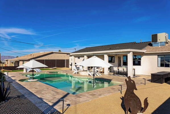 A swimming pool with lounge chairs and umbrellas, a patio area, and a building with a tiled roof.