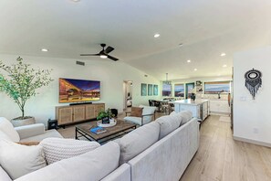 A spacious living area with a sofa, coffee table, and a television. There is a kitchen area with a dining table and chairs. - Updated Oasis w/ Private Yard, BBQ & Hot Tub (Lake Havasu City)