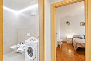 A modern bathroom with a washing machine, bidet, and toilet. - Riva's Garden Home (Riva del Garda)