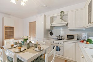 Una cocina moderna con armarios blancos, una mesa de comedor dispuesta con platos y tazas, un microondas y una estufa.