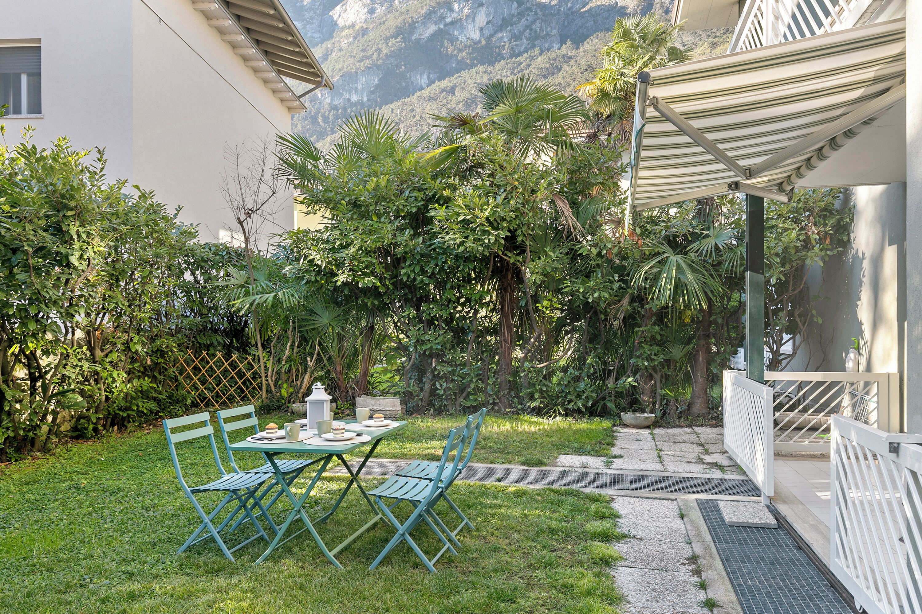 Eine Terrasse mit Tisch und Stühlen, umgeben von üppiger Vegetation und Blick auf Berge.