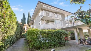 A multi-story building with a covered walkway and a paved pathway leading to the entrance. - Riva's Garden Home (Riva del Garda)
