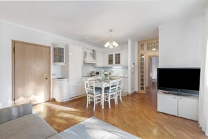 Una cocina moderna con armarios blancos, una mesa de comedor con sillas, un televisor de pantalla plana y una puerta de madera.